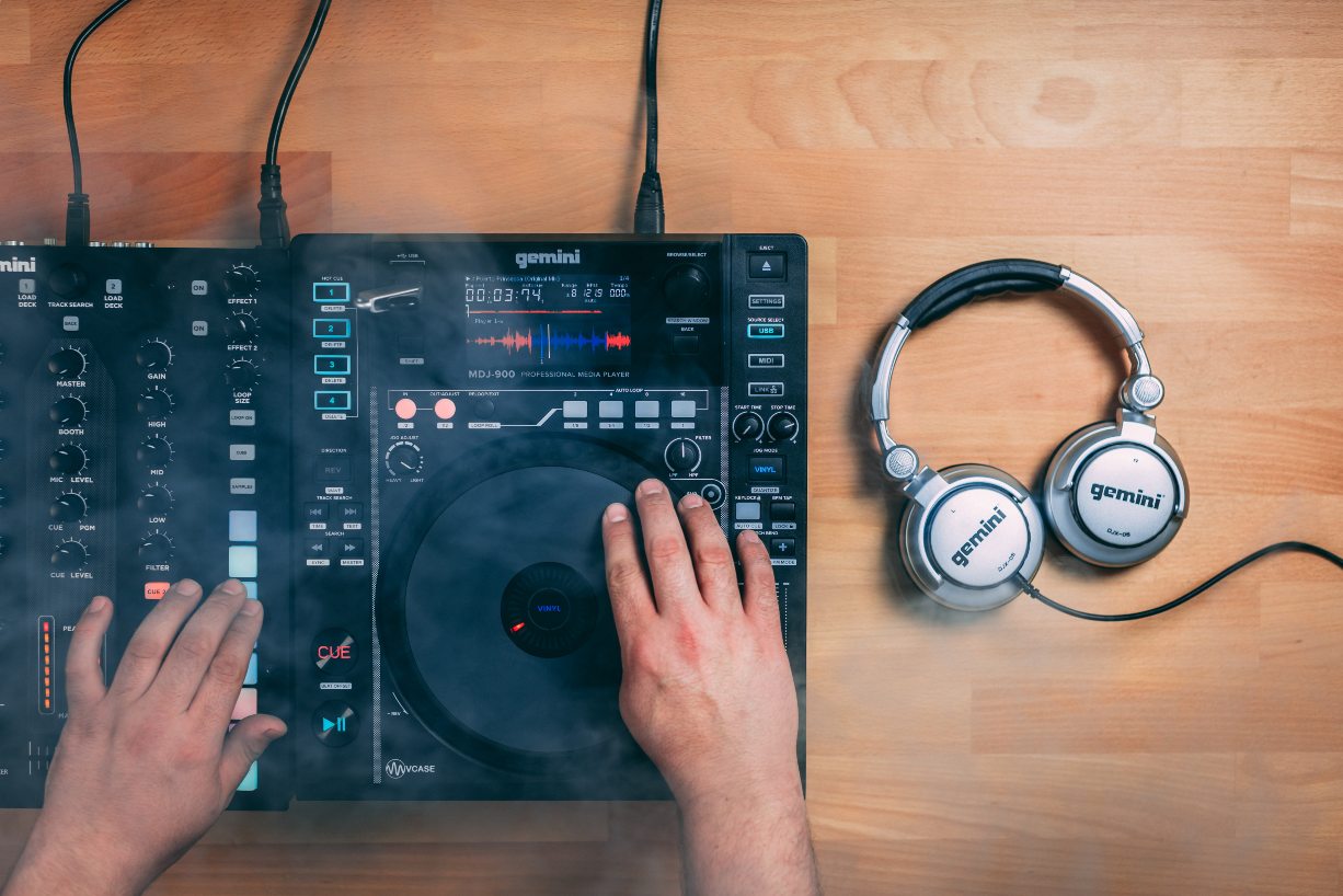 Hands operating a DJ mixer with Gemini Sound headphones